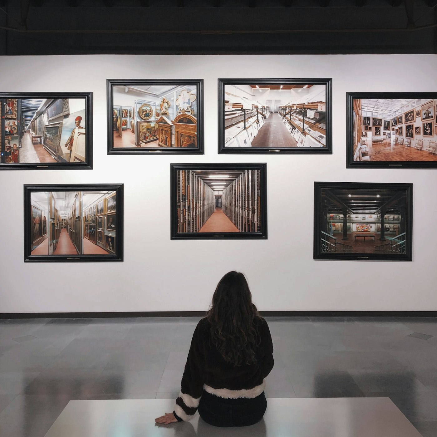 A visitor seated before a wall of framed photographs in a gallery