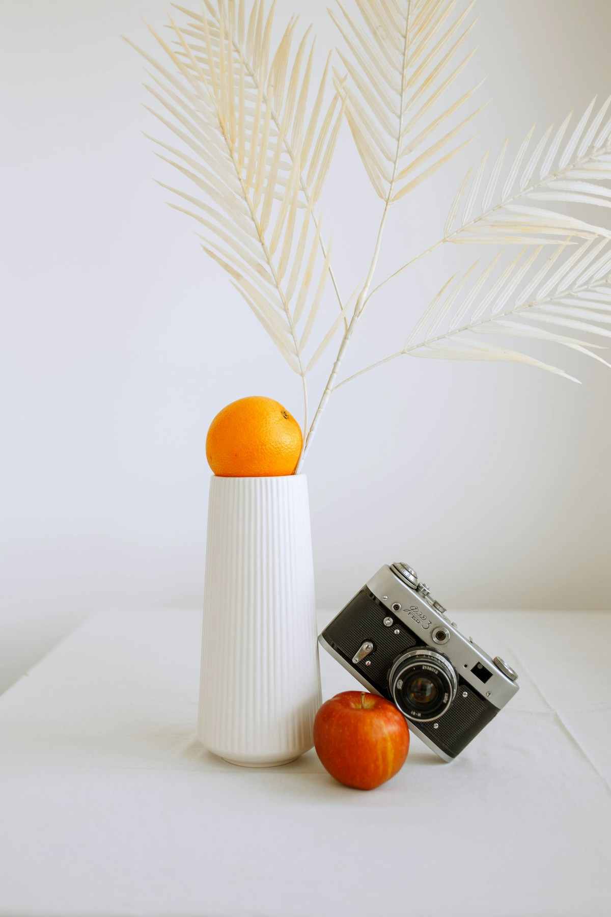 Minimal still life of an orange on a white vase